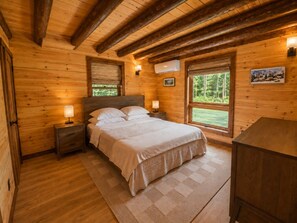 A wooden cabin bedroom with a bed, bedside lamps, a window, and a wall-mounted air conditioner.