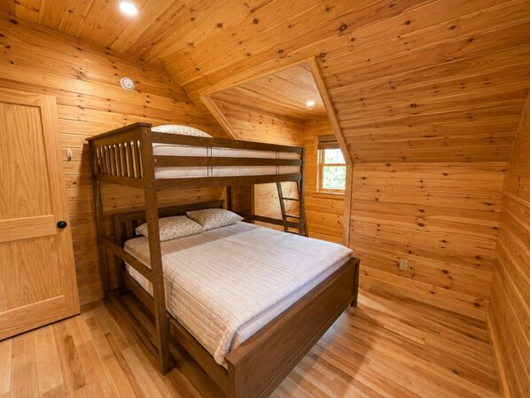 A wooden bunk bed in a cabin-style room with a sloped ceiling and wooden walls.