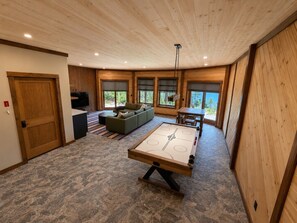 A room with a pool table, a sofa, and a view of the outdoors.