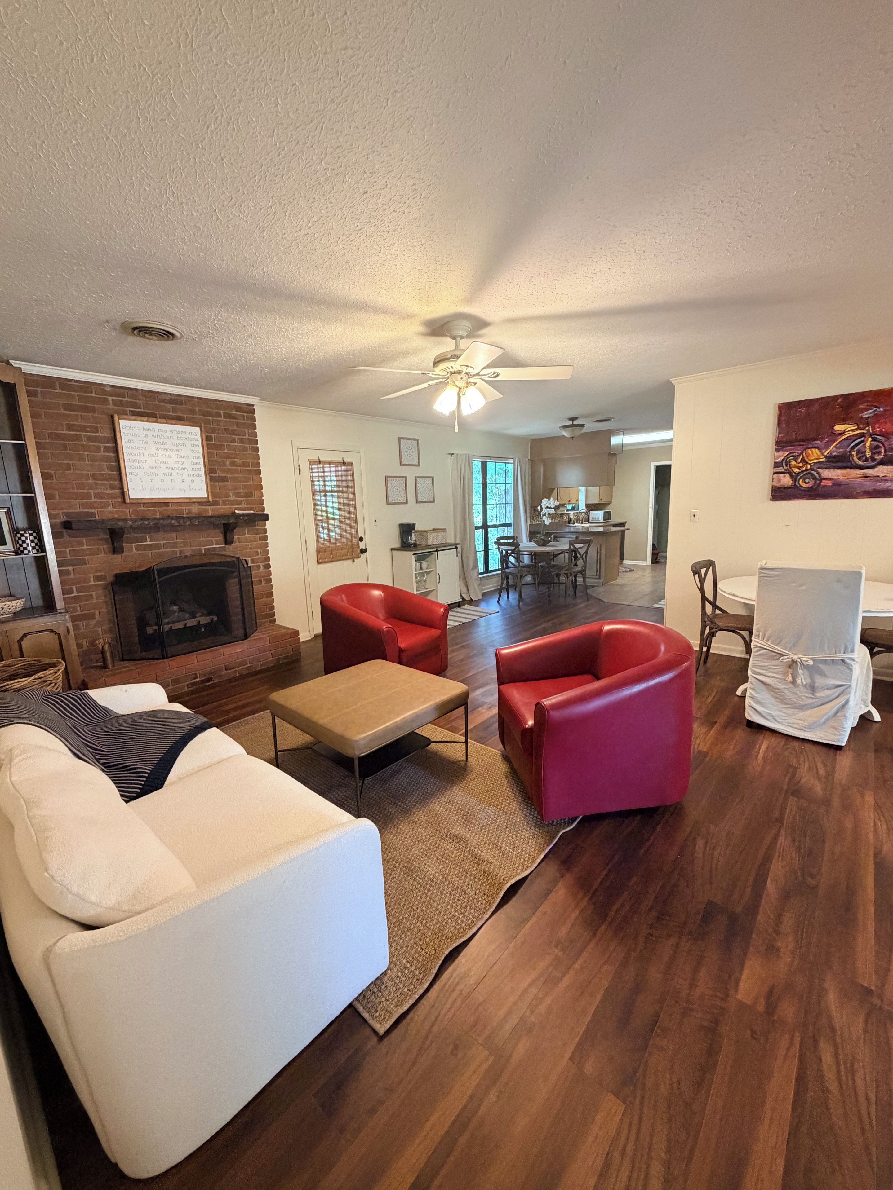 A living room with a fireplace, red chairs, a white sofa, and a ceiling fan.