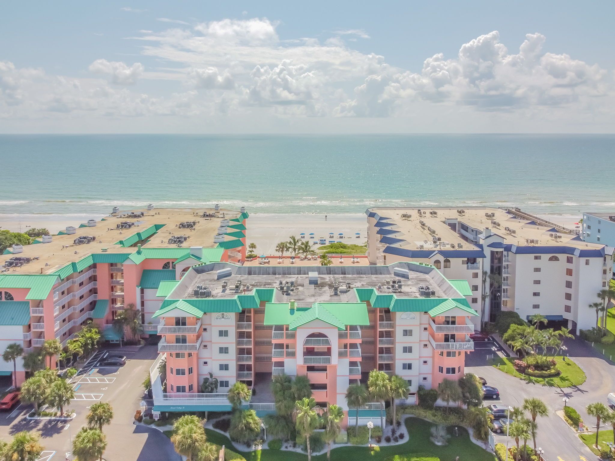 A beachfront hotel with multiple buildings, a parking lot, and a beach area.