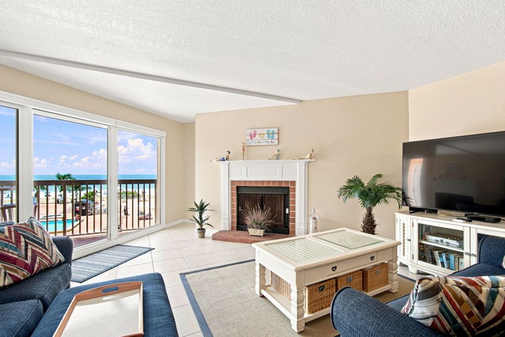 Sala de estar com lareira, televisão e vista para a praia.