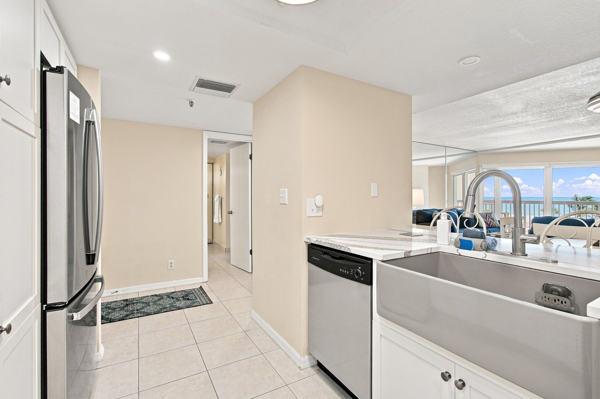 A modern kitchen with a built-in dishwasher, stainless steel appliances, and a view of the ocean through large windows.