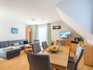 Una sala de estar moderna con sofá, mesa de comedor, sillas, televisor y estantería.