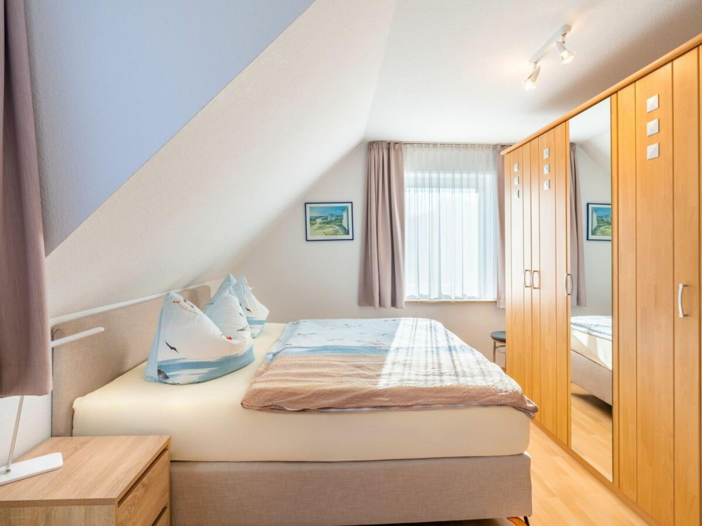 Een slaapkamer met een bed, een houten garderobe, een nachtkastje en een raam met gordijnen.