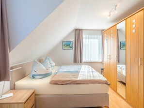 A bedroom with a bed, a wooden wardrobe, a bedside table, and a window with curtains. - Holiday Apartment With 1 Bedroom (Heringsdorf)