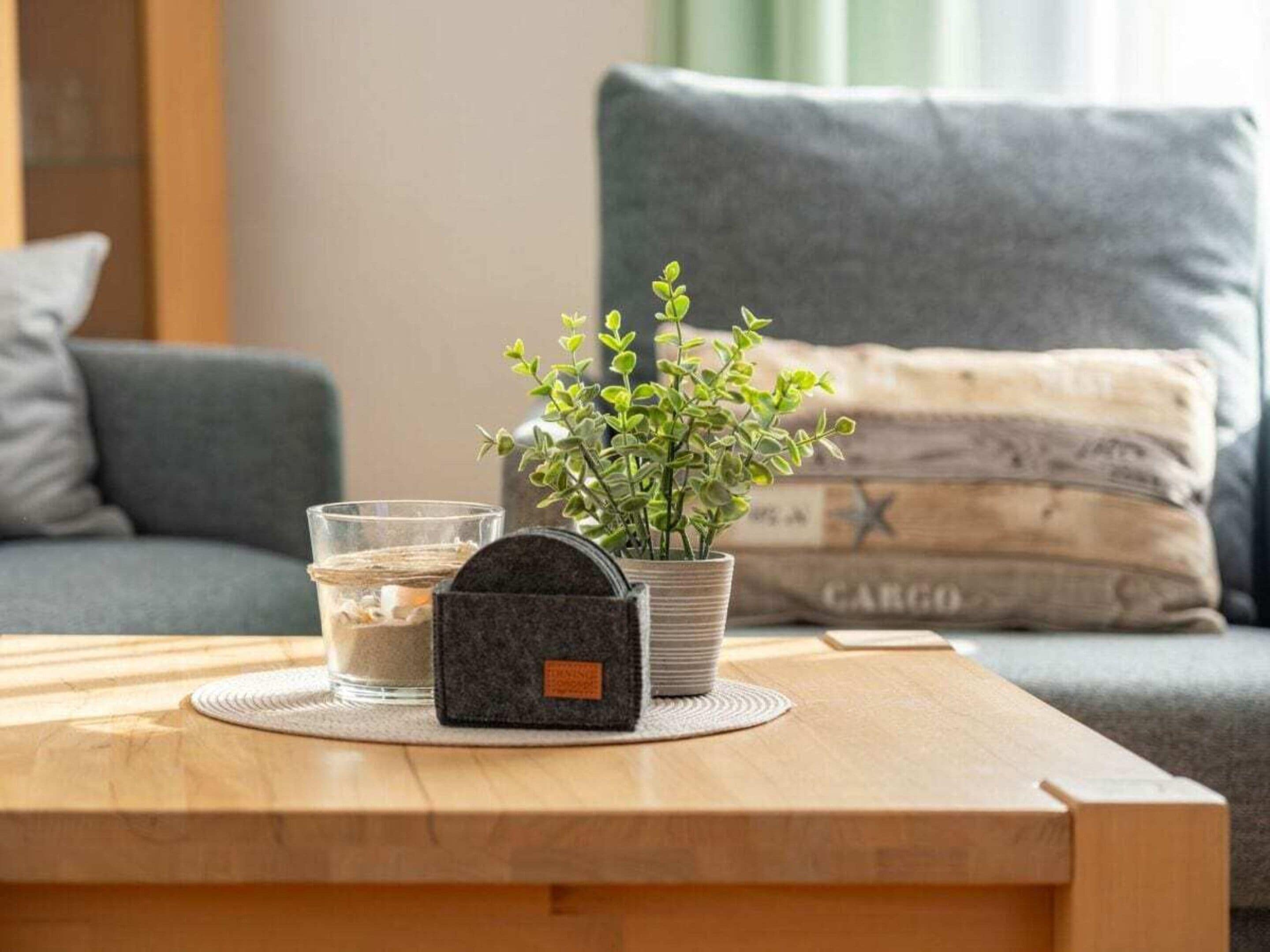 A wooden table with a glass of water, a small potted plant, and a black object on a coaster.