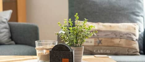 A wooden table with a glass of water, a small potted plant, and a black object on a coaster.