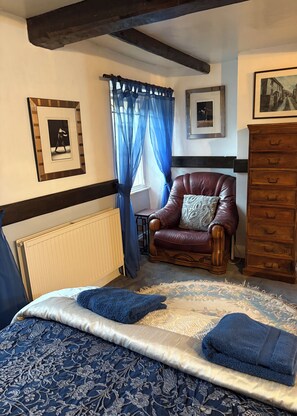 A bedroom with a bed, a leather armchair, a dresser, and a window with blue curtains. - Beautiful 400 yr old thatch house.Sleeps 11, dog friendly,close to beaches,moors (Combeinteignhead)