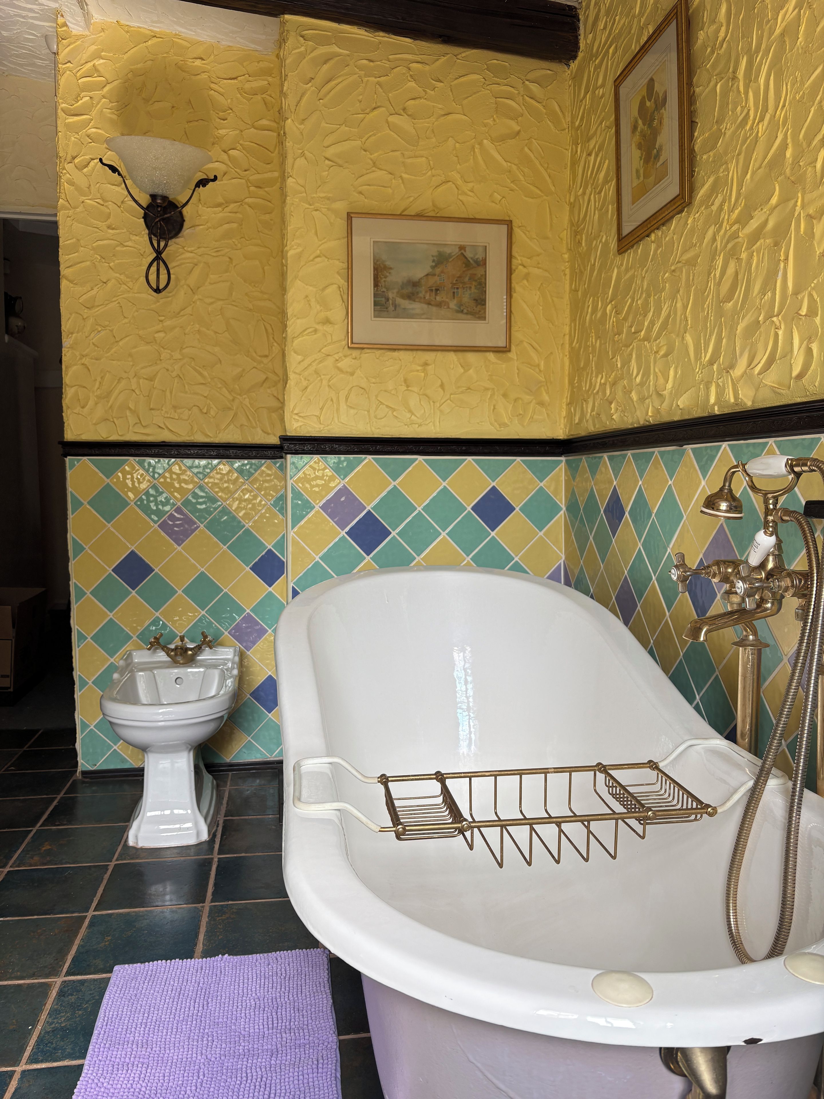 A bathroom with a bathtub, a white sink, a wall-mounted light fixture, and a tiled wall with a diamond pattern.
