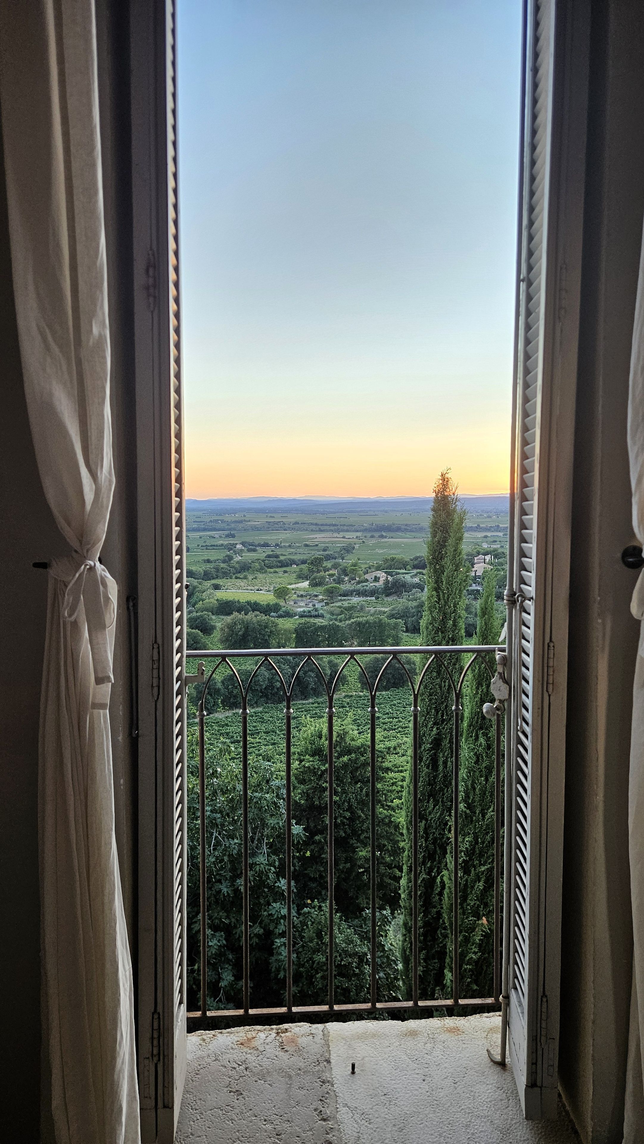 A balcony with a metal railing overlooking a landscape with trees and distant buildings.