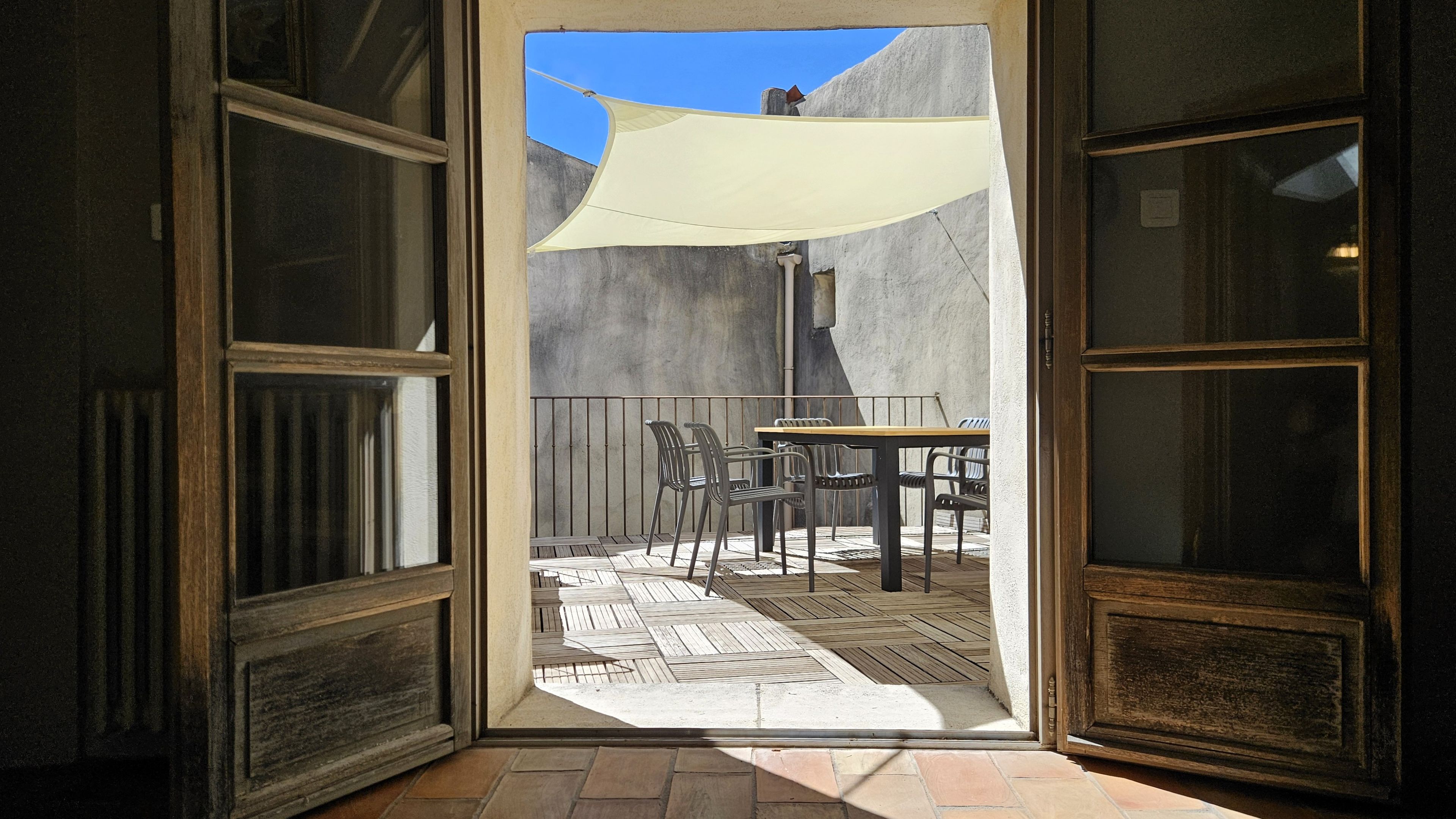 An open doorway leading to a patio with a table and chairs, a white shade sail, and a concrete wall.