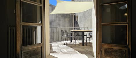 An open doorway leading to a patio with a table and chairs, a white shade sail, and a concrete wall.