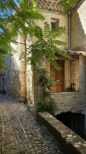 A stone building with a wooden door and a window, surrounded by cobblestone pavement. - Charming 3-bedroom house with panoramic views in peaceful Séguret (Séguret)