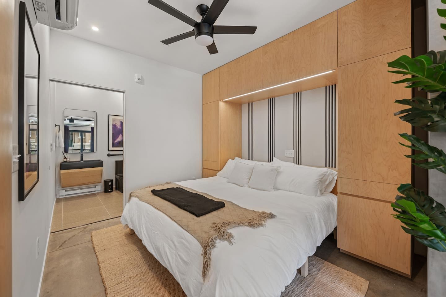 A modern bedroom with a bed, a ceiling fan, a wooden panel wall, and a large mirror.