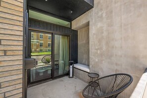 A balcony with a view of a building, a chair, and a small table. - Modern King Suite at City Park | Walk to Downtown (Manhattan)