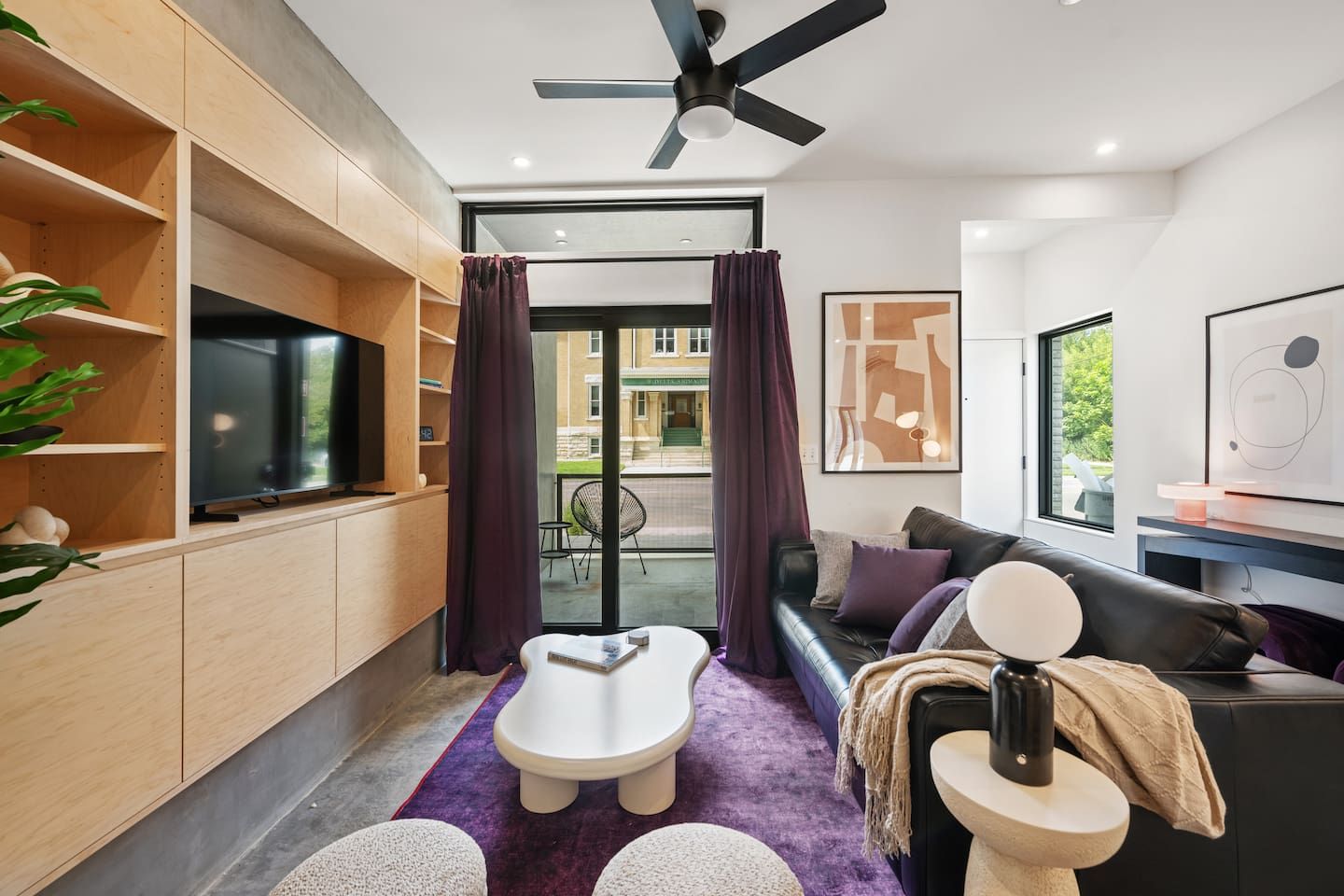 A modern living room with a flat-screen TV, a ceiling fan, a sofa, a coffee table, and a small seating area with a purple rug.