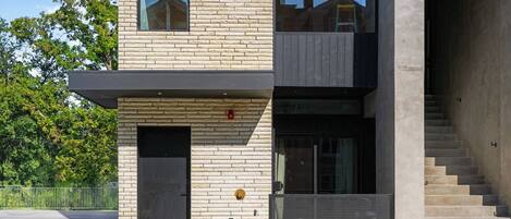 Un edificio moderno de dos plantas con fachada de piedra, una puerta negra y una escalera visible que conduce al segundo piso.