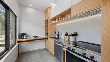 A modern kitchen with a built-in oven, stainless steel appliances, wooden shelves, and a window providing natural light.