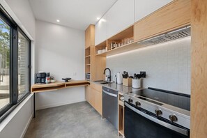 A modern kitchen with a built-in oven, stainless steel appliances, wooden shelves, and a window providing natural light. - Modern King Suite at City Park | Walk to Downtown (Manhattan)
