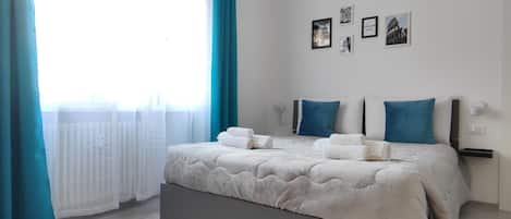 A bedroom with a bed, curtains, wall-mounted air conditioning, and framed pictures.