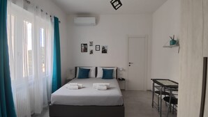 Hotelkamer met een bed, twee kussens, een nachtkastje, een bureau, een stoel, een deur en een raam met gordijnen.