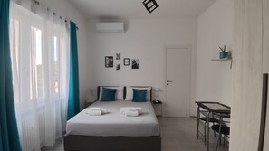 Ein Hotelzimmer mit einem Bett, zwei Kissen, einem Nachttisch, einem Schreibtisch, einem Stuhl, einer Tür und einem Fenster mit Vorhängen.