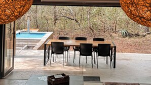 An indoor dining area with a pool view, featuring a table with chairs and two large spherical light fixtures. - Luxury Bush Villa | Private Pool, Hot Tub in Marloth at the Kruger National Park (Marloth Park)