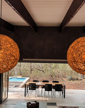 An indoor dining area with a pool view, featuring a table with chairs and two large spherical light fixtures. - Luxury Bush Villa | Private Pool, Hot Tub in Marloth at the Kruger National Park (Marloth Park)