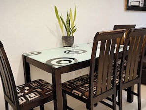 Een eettafel met een glazen blad en zwarte ronde patronen, omringd door vier stoelen met gestreepte kussens.