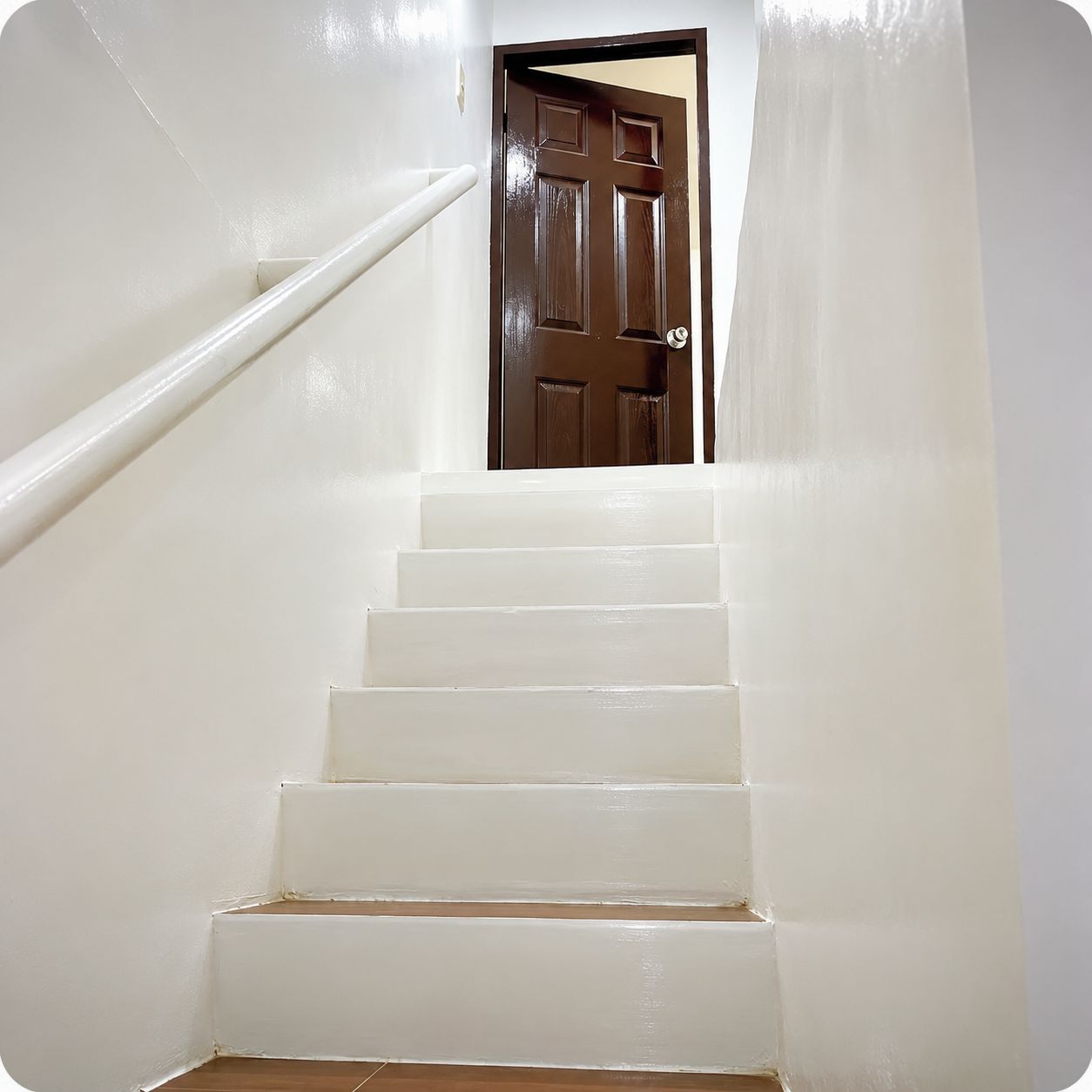 Eine weiße Treppe führt zu einer braunen Tür.
