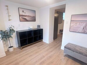 A modern living room with a wooden floor, a black console table, and two framed pictures on the walls. - Elegant Trinity Bellwoods 1BR2BA Parkside Retreat (Toronto)