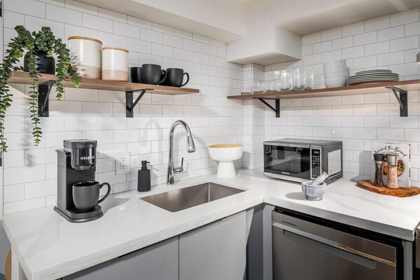 A modern kitchen with white subway tiles, stainless steel appliances, and wooden shelves.