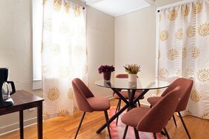 Ein Zimmer mit einem runden Glastisch, vier Stühlen, einer Kaffeemaschine und zwei Blumentöpfen.