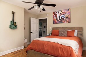 Ein Schlafzimmer mit einem Bett, einem Deckenventilator, einer Gitarre und einem Gemälde.