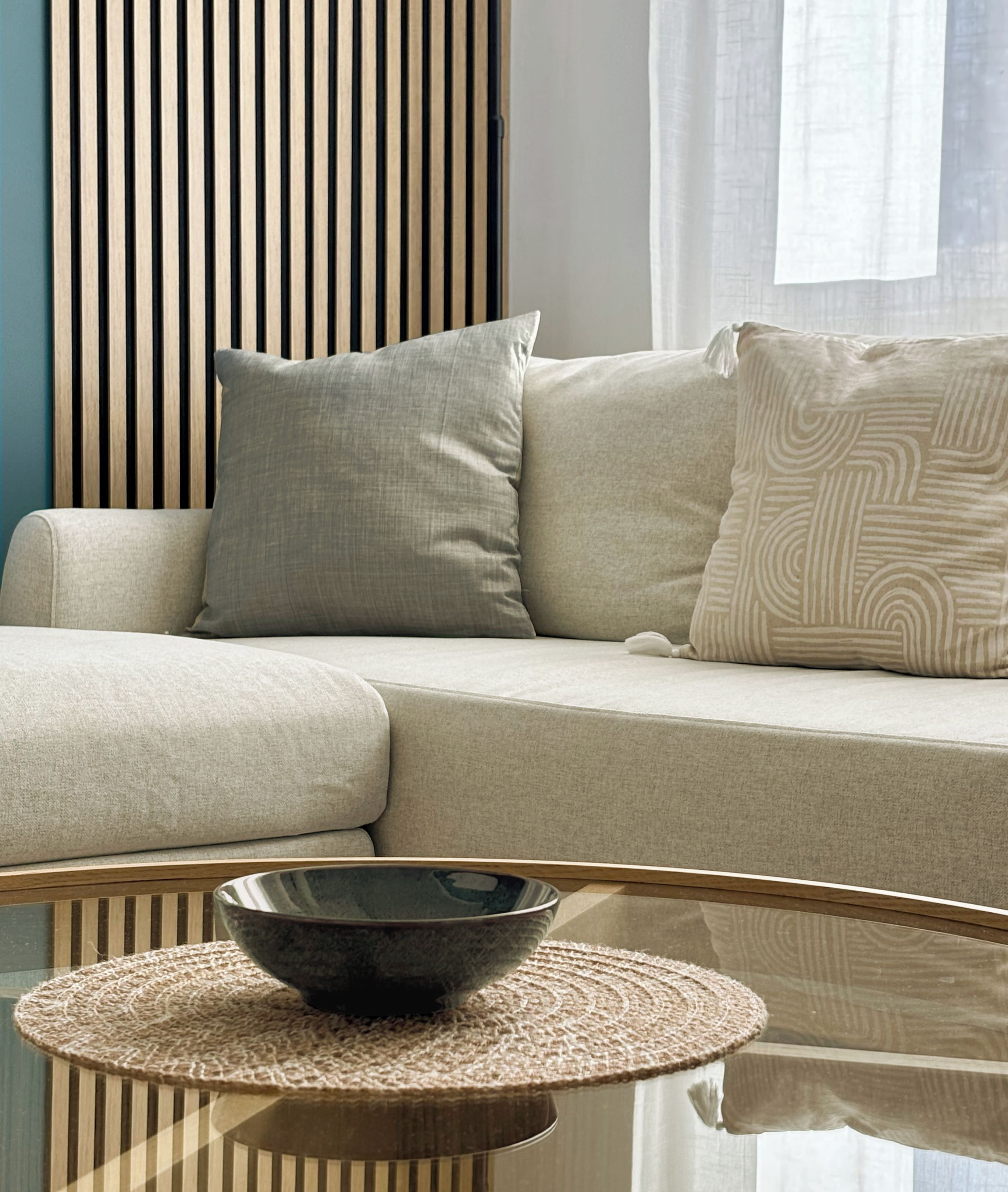 Un salon moderne avec un canapé, des coussins et une table basse en verre sur laquelle est posé un bol.