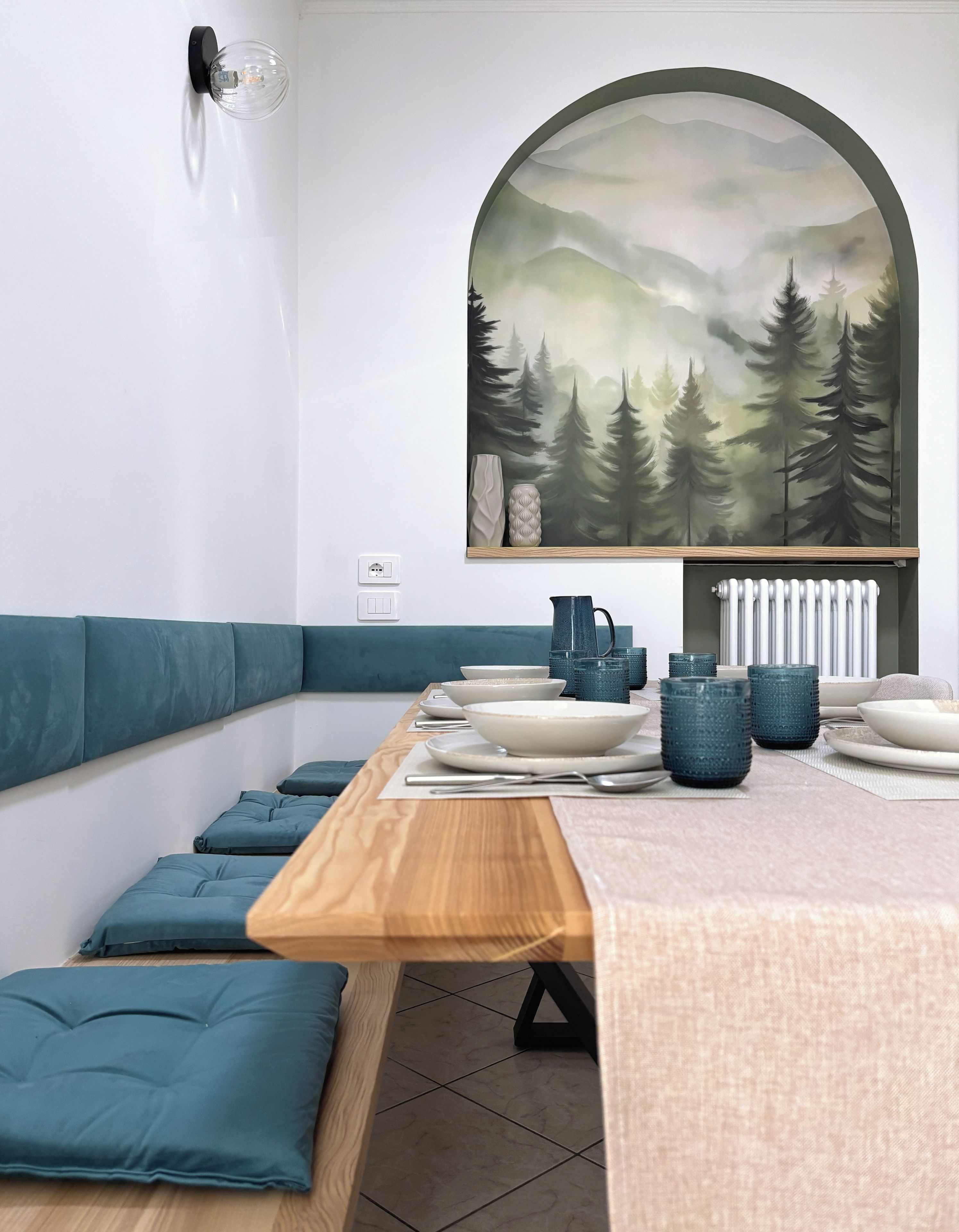 A modern dining area with a wooden table, teal cushions, and a large landscape painting above.