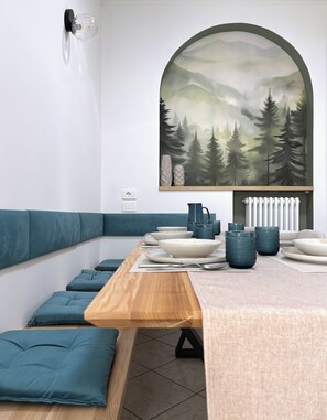 Ein moderner Essbereich mit einem Holztisch, Kissen in Türkis und einem großen Landschaftsbild darüber.