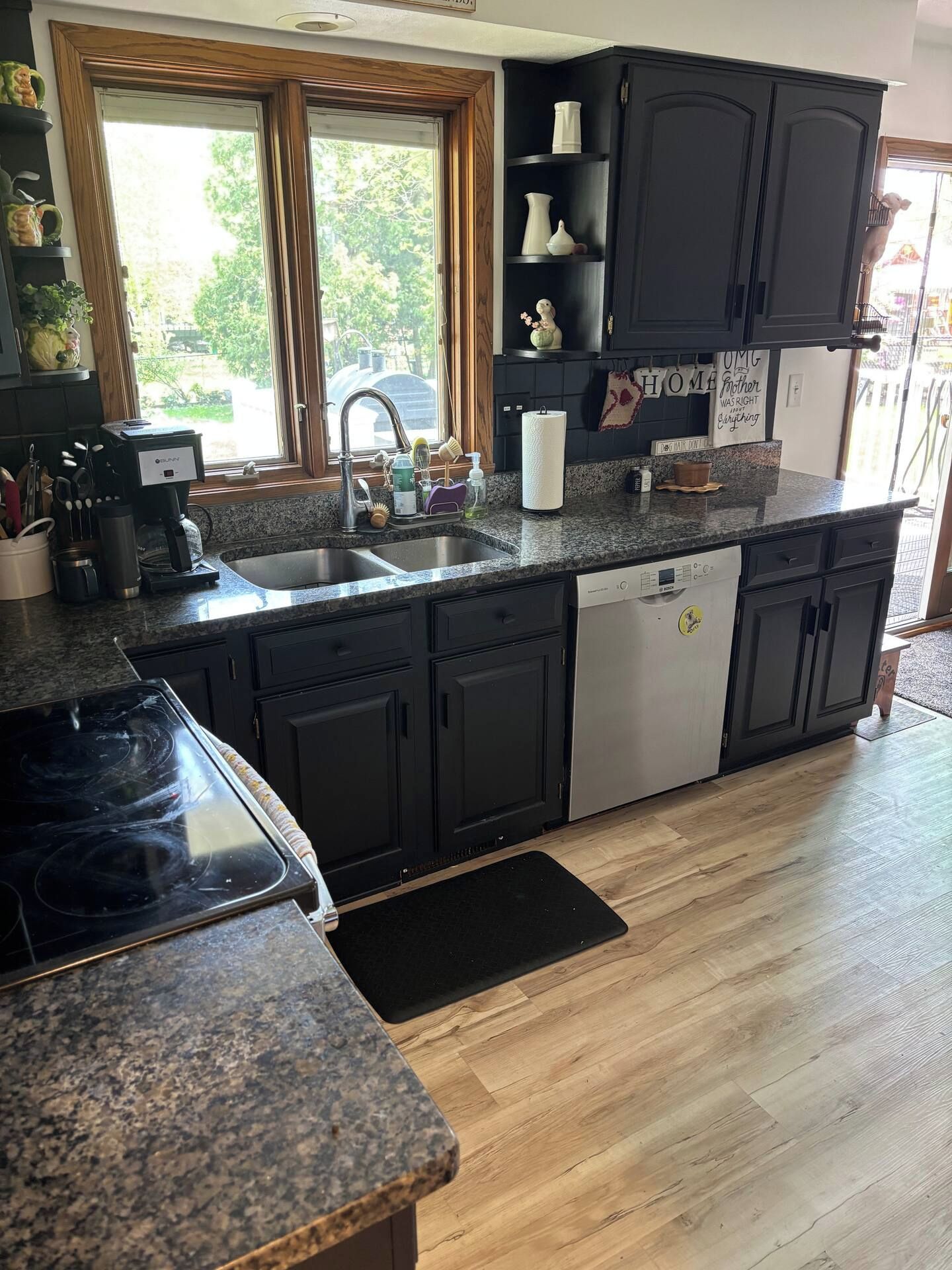 A kitchen with dark cabinets, a dishwasher, a stove, and a window with a view of greenery.