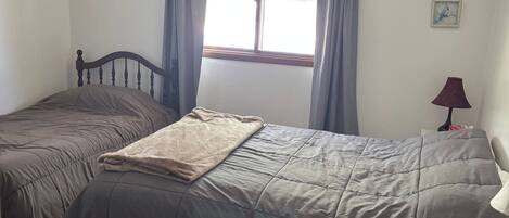 Une chambre avec deux lits simples, une fenêtre avec des rideaux, une lampe et une petite table.