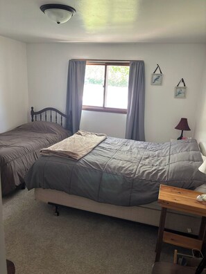 A bedroom with two single beds, a window with curtains, a lamp, and a small table.