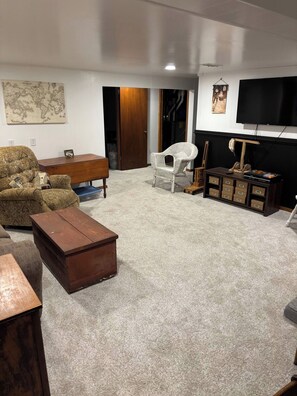 A living room with a sofa, a wooden coffee table, a wicker chair, a television, and a map on the wall.