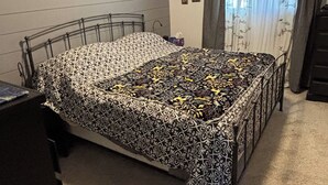 Une chambre à coucher avec un lit en métal, une couvre-lit à motifs, un sol recouvert de moquette, une commode et une fenêtre avec des rideaux.