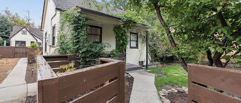 A residential property with a paved driveway, wooden gates, and a garden area with trees and shrubs.