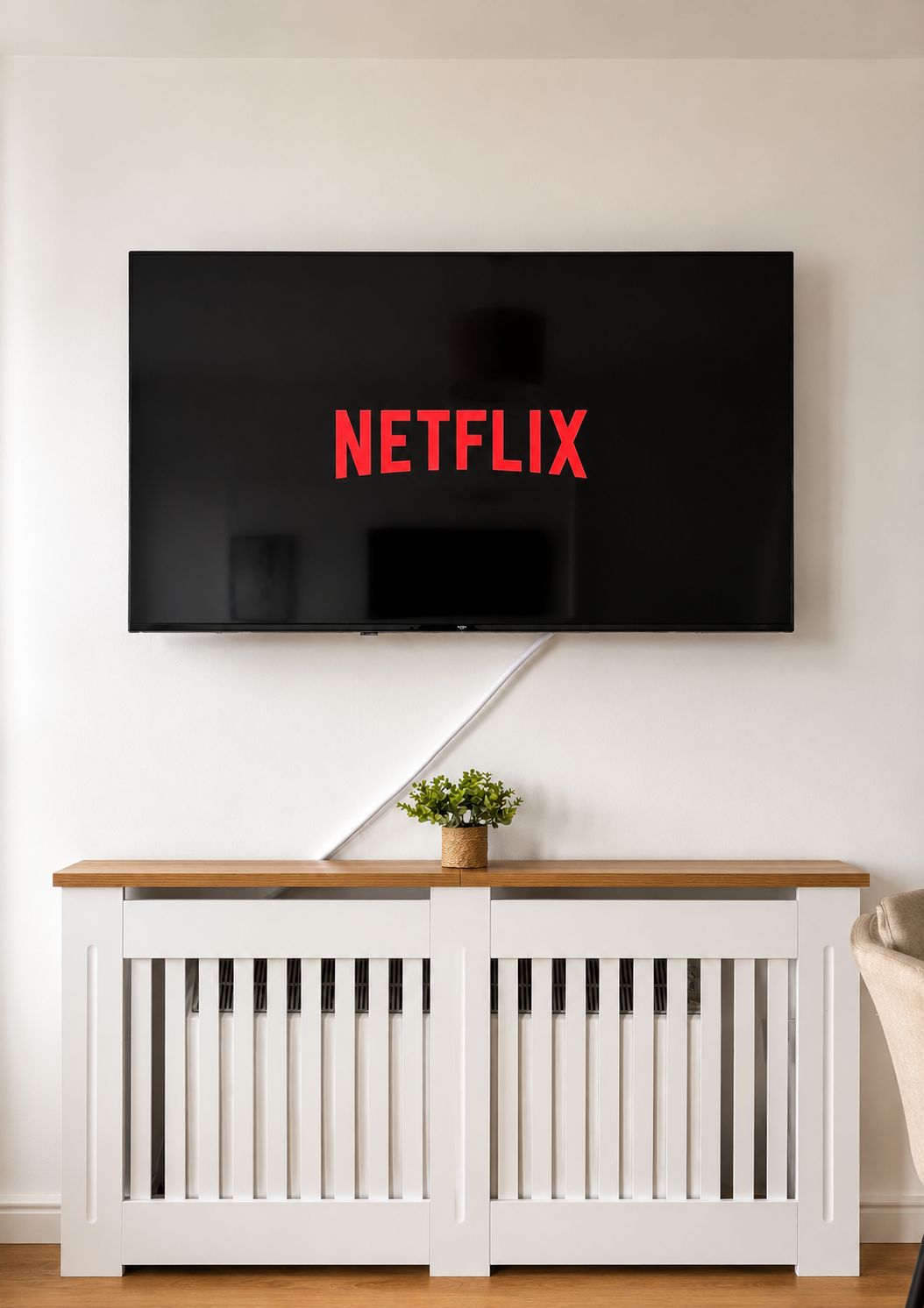 Ein Fernseher, der an einer Wand über einer weißen Konsole befestigt ist, auf der sich eine Pflanze befindet.