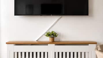Ein Fernseher, der an einer Wand über einer weißen Konsole befestigt ist, auf der sich eine Pflanze befindet.