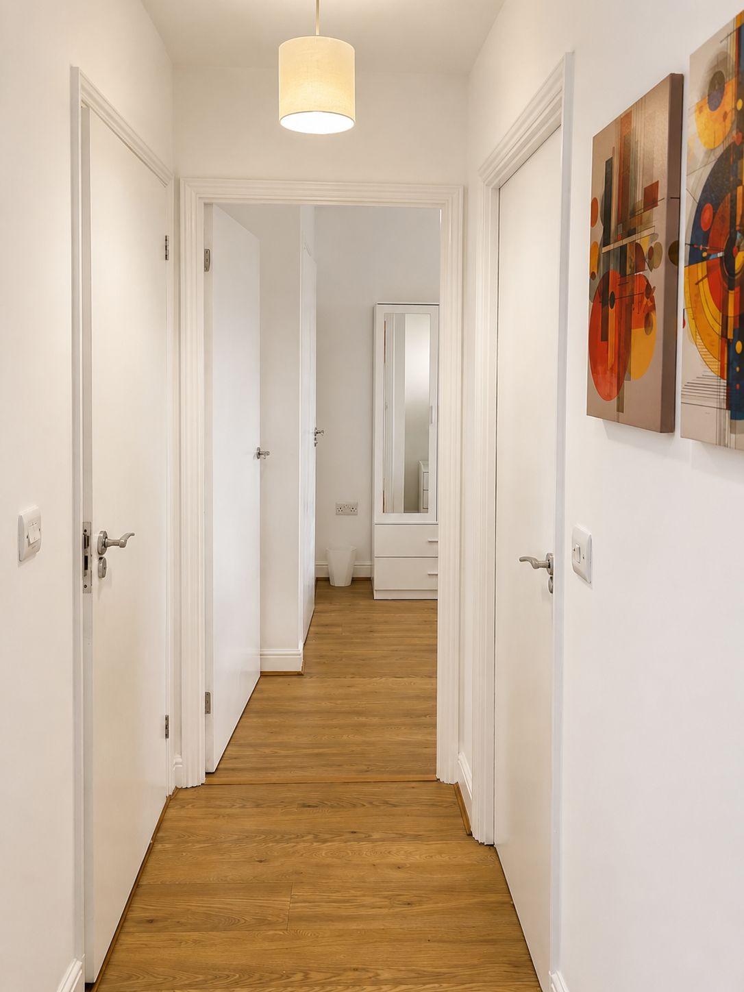 Ein Flur mit Holzboden, weißen Türen, einer Pendelleuchte und zwei Wandbildern.