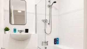 Casa de banho moderna com lavatório branco, espelho, chuveiro e banheira.