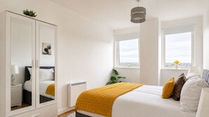 Quarto com cama, guarda-roupa, radiador, janela com vista e luminária suspensa.