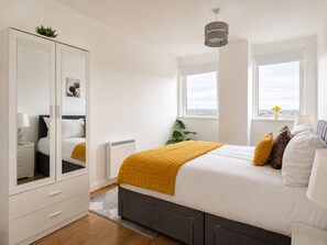 A bedroom with a bed, a wardrobe, a radiator, a window with a view, and a hanging light fixture. - Modern 2 bed 2 bath - 1 Min to Station - Skyline View - Sleeps 5 (Ilford)